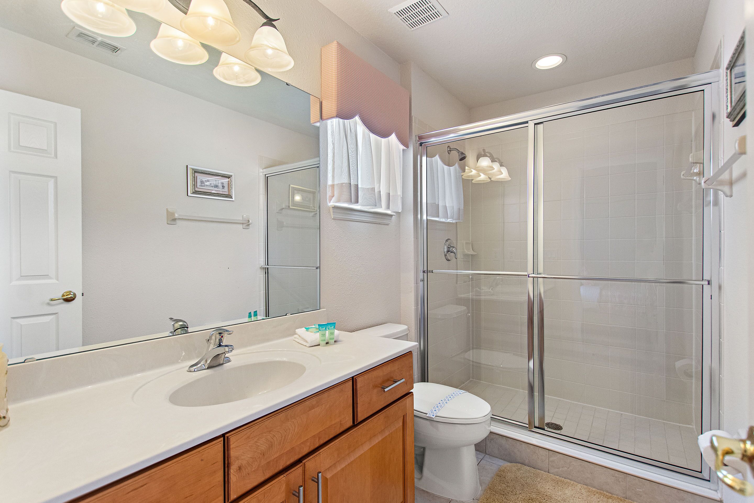 Une salle de bain avec un meuble-lavabo à deux vasques, un grand miroir, une douche avec des portes en verre et des toilettes.