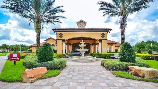 Entrada de hotel com uma fonte central, palmeiras e um jardim bem cuidado.