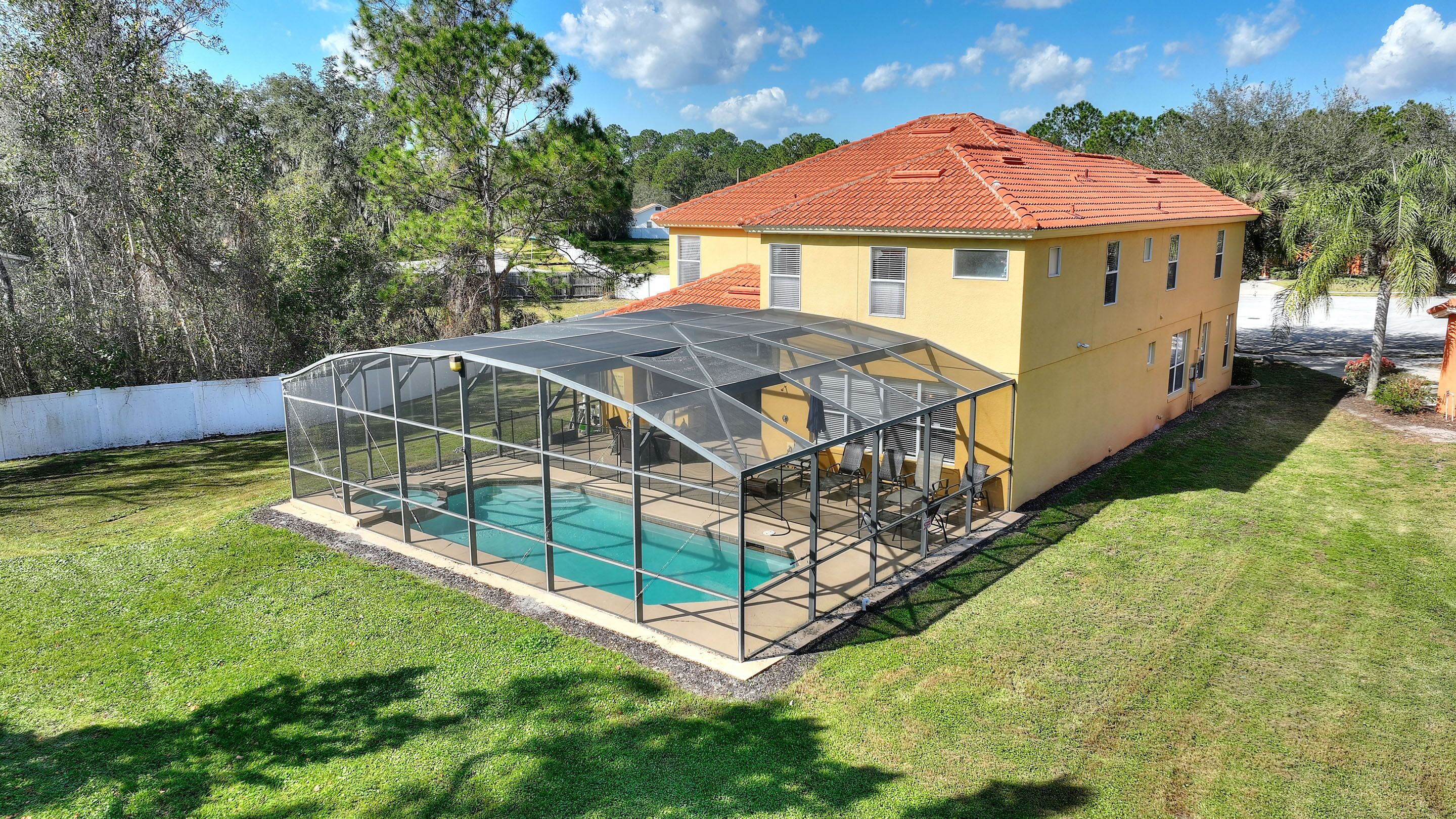 A house with a swimming pool covered by a glass enclosure, surrounded by a well-maintained lawn and trees.