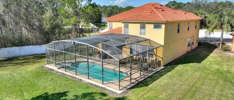 A house with a swimming pool covered by a glass enclosure, surrounded by a well-maintained lawn and trees.