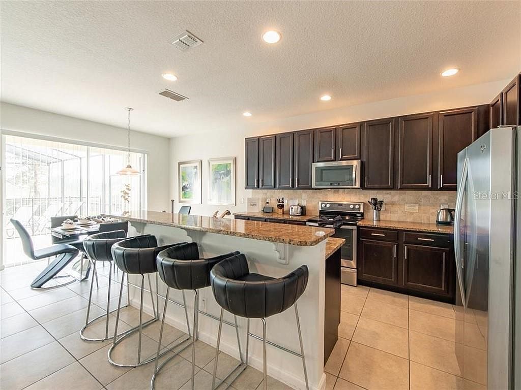 A modern kitchen with dark cabinets, stainless steel appliances, and a central island with bar stools.