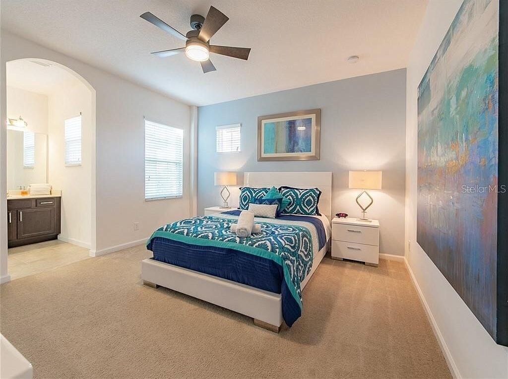 Une chambre à coucher avec un lit, des tables de chevet, un ventilateur de plafond et un grand tableau accroché au mur.