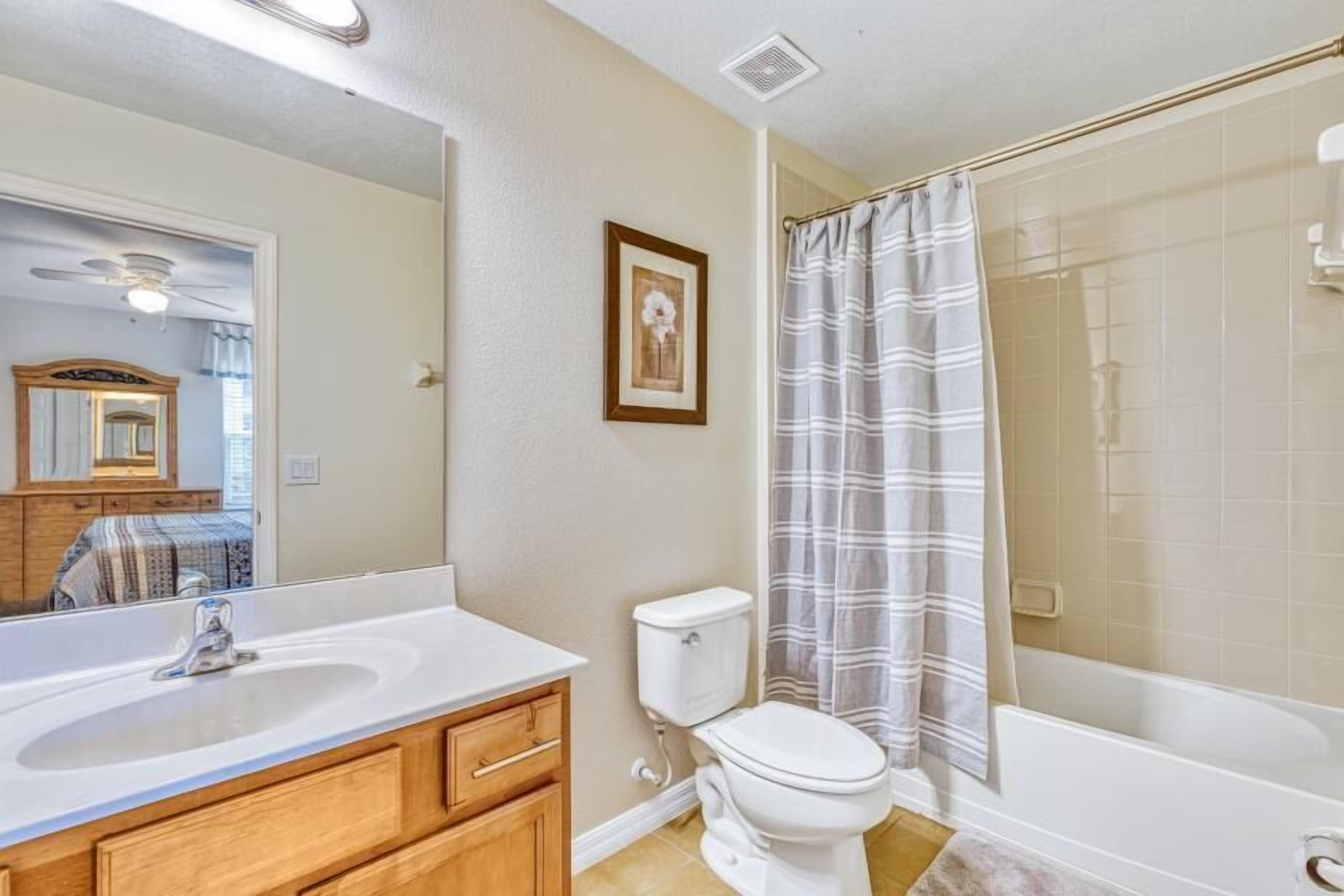 A bathroom with a white sink, wooden vanity, a toilet, and a shower with a striped curtain.