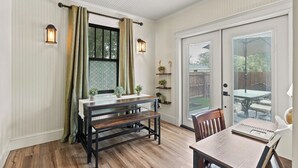 Un comedor con banco y mesa de madera, una ventana con cortinas y un cerramiento de vidrio corredizo que da al exterior.