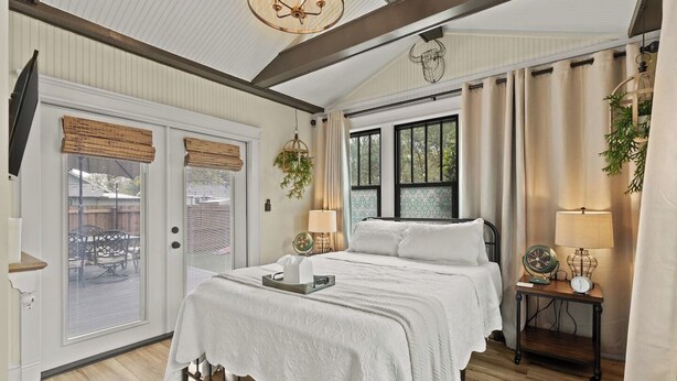 Un dormitorio con una cama, lámparas de noche, una ventana con cortinas y una puerta con persianas.