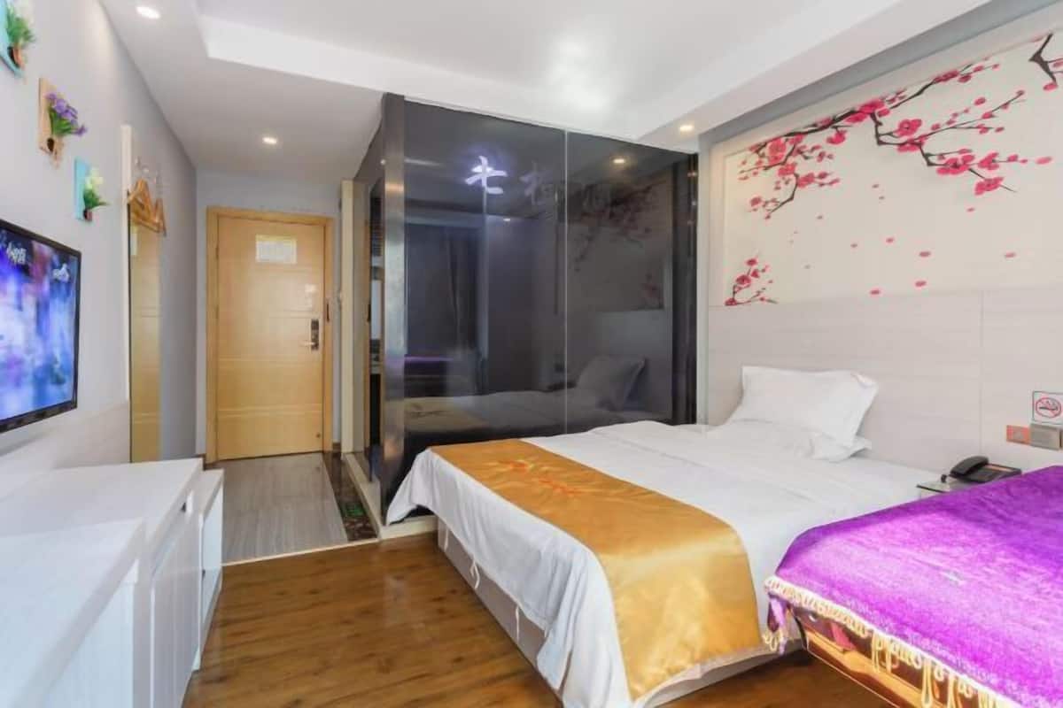 A hotel room with a bed, a TV, a wooden floor, and a wall with a floral design.
