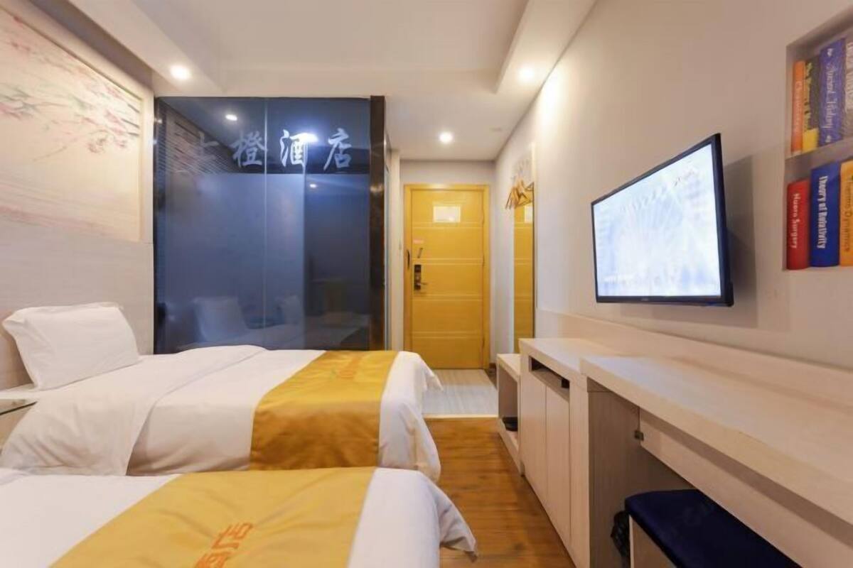 A hotel room with two beds, a television, a bookshelf, and a door leading to another room.
