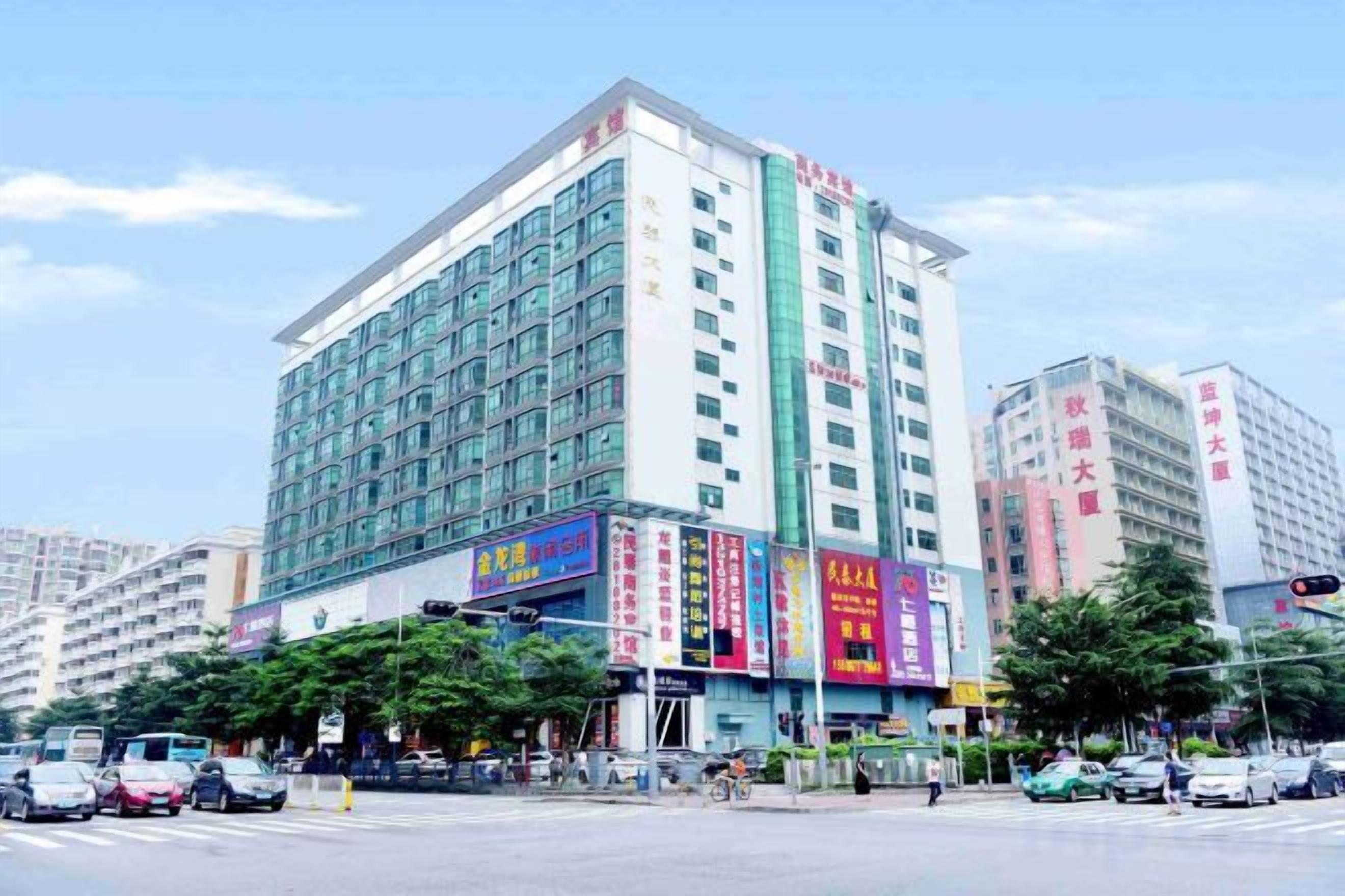 A multi-story hotel with a prominent signage on the facade, a street in front with parked cars, and other buildings in the background.