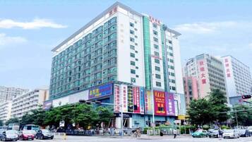 A multi-story hotel with a prominent signage on the facade, a street in front with parked cars, and other buildings in the background.