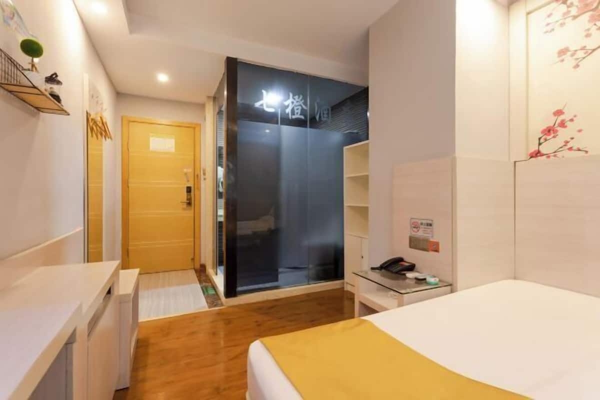 A hotel room with a bed, a desk, a wardrobe, and a shower area.