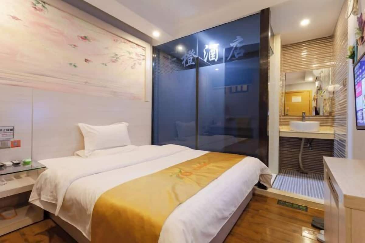 A hotel room with a bed, a glass partition, a bathroom with a sink, and a decorative wall.