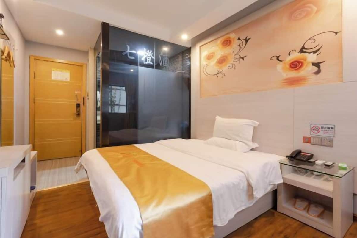 A hotel room with a bed, bedside table, and a wall with floral artwork.