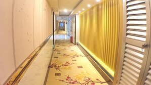 A hotel corridor with a patterned carpet, a yellow wall with vertical blinds, and a door with horizontal blinds. - Seven Orange Hotel (Shenzhen North Station Minzhi) (Shenzhen)