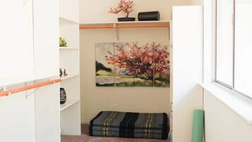 Una habitación con pared blanca, un cuadro de un árbol de cerezo, un banco con estampado negro y dorado, y un armario blanco.