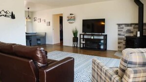 Ein Wohnzimmer mit braunem Ledersofa, einem karierten Sofa, einem Flachbildfernseher, einem Kamin und einem Deckenventilator.