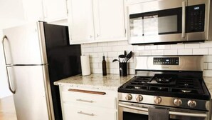 Eine Küche mit einem Edelstahlkühlschrank, einer Mikrowelle, einem Gasherd und einem Backofen.