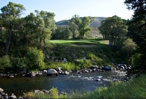 Ein Golfplatz mit einem Fluss, der sich hindurchschlängelt, umgeben von Bäumen und Hügeln.