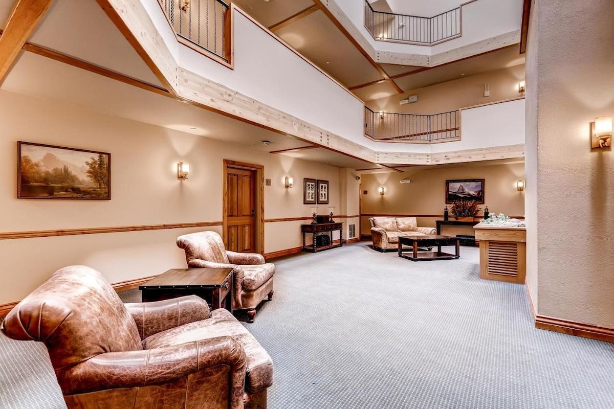 A spacious interior with a high ceiling, a central seating area with leather sofas, a wooden coffee table, and a small side table.