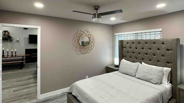 Une chambre avec une tête de lit capitonnée, un ventilateur de plafond et un grand miroir au mur.