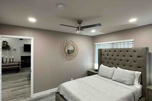 A bedroom with a tufted headboard, a ceiling fan, and a large mirror on the wall. - 5 star two bedroom rental (Las Vegas)