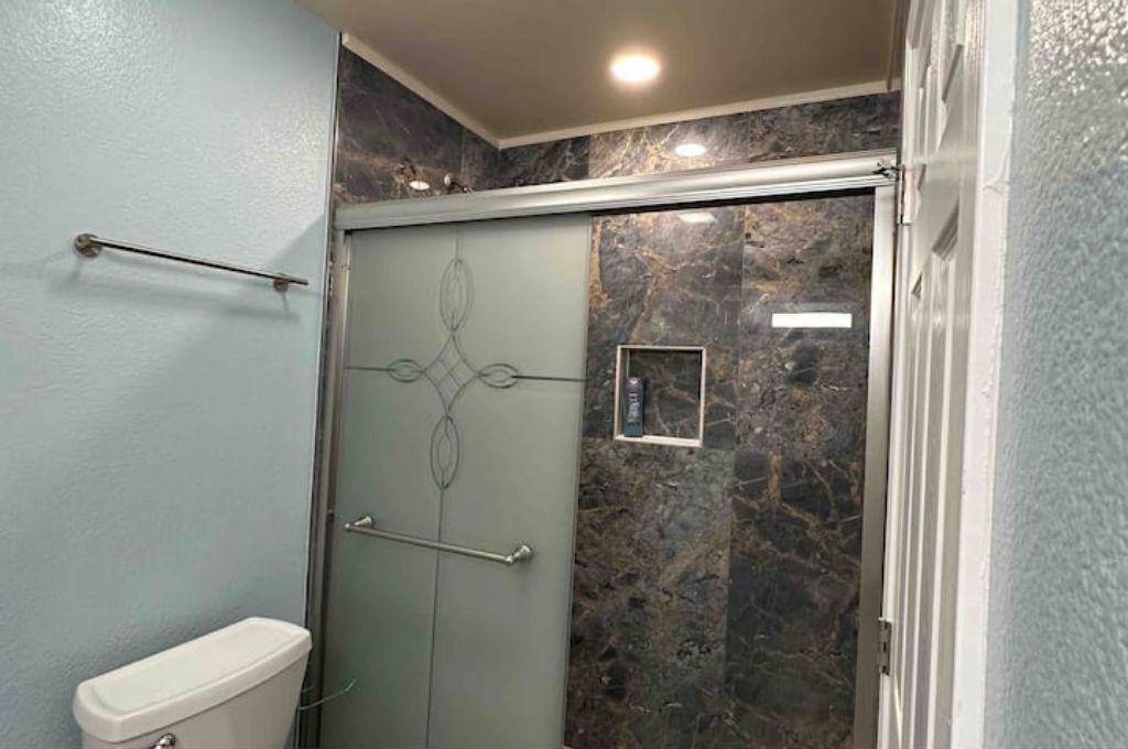 Un baño con inodoro, cabina de ducha de vidrio y paredes de mármol.