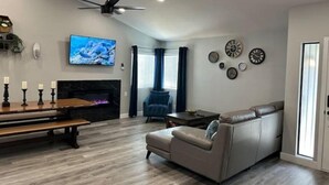 Un salon moderne avec une cheminée, un canapé, un téléviseur et un ventilateur de plafond.