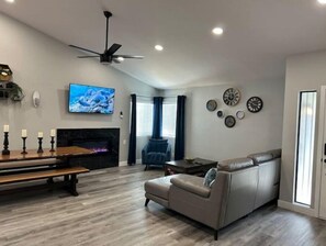 A modern living room with a fireplace, a sofa, a TV, and a ceiling fan.