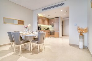 Un espace repas moderne avec une table en marbre et des chaises recouvertes d’un tissu gris, donnant sur une cuisine dotée de meubles en bois et d’un four encastré.