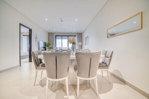 A modern dining area with a round table and six chairs, a large mirror, and a view of a balcony.
