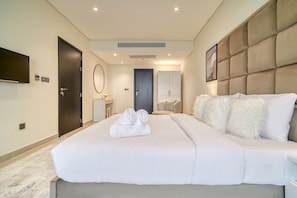 A modern hotel room with a large bed, a flat-screen TV, a wardrobe, and a bathroom visible through an open door.