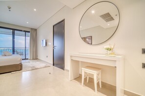 Une chambre d’hôtel moderne avec un grand lit, un miroir rond, une console blanche et une vue sur l’extérieur.