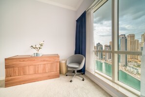 A room with a wooden dresser, a grey office chair, a small plant, and a large window with a city view.