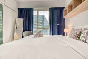 A hotel room with a bed, a chair, a desk, a lamp, and a window with curtains.