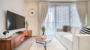 Ein modernes Wohnzimmer mit Flachbildfernseher, Couch, Holz-Couchtisch und einem großen Fenster mit transparenten Vorhängen.