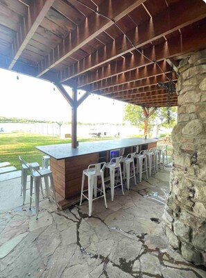 An outdoor bar area with a stone floor, wooden ceiling, and white bar stools. - Lakefront Retreat Hot Tub +Private Dock - Sleeps 12 - Eagle Mountain Lake (Fort Worth)