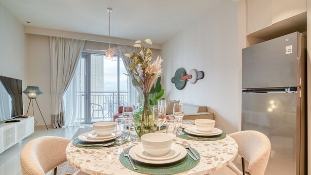 A dining area with a round table set for four, surrounded by cushioned chairs. A modern refrigerator is visible to the right.