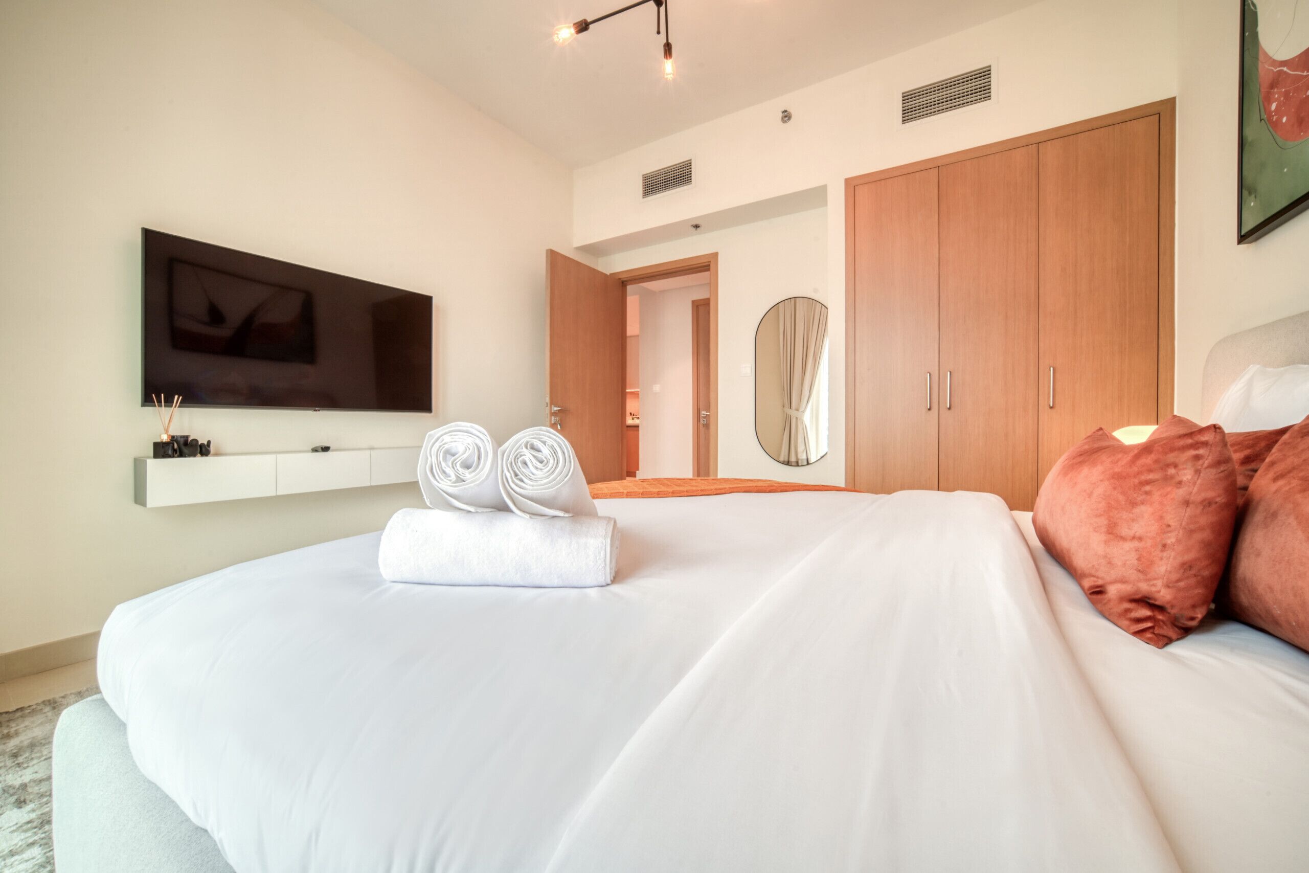 A modern hotel room with a large bed, a flat-screen TV mounted on the wall, and a wooden wardrobe.