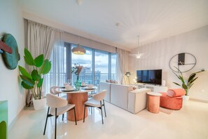 A modern living room with a dining area, a kitchen, and a large window offering a city view.