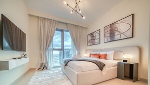Ein modernes Schlafzimmer mit einem großen Bett, einem Nachttisch, einem an der Wand montierten Fernseher und Blick auf die Stadt durch große Fenster.