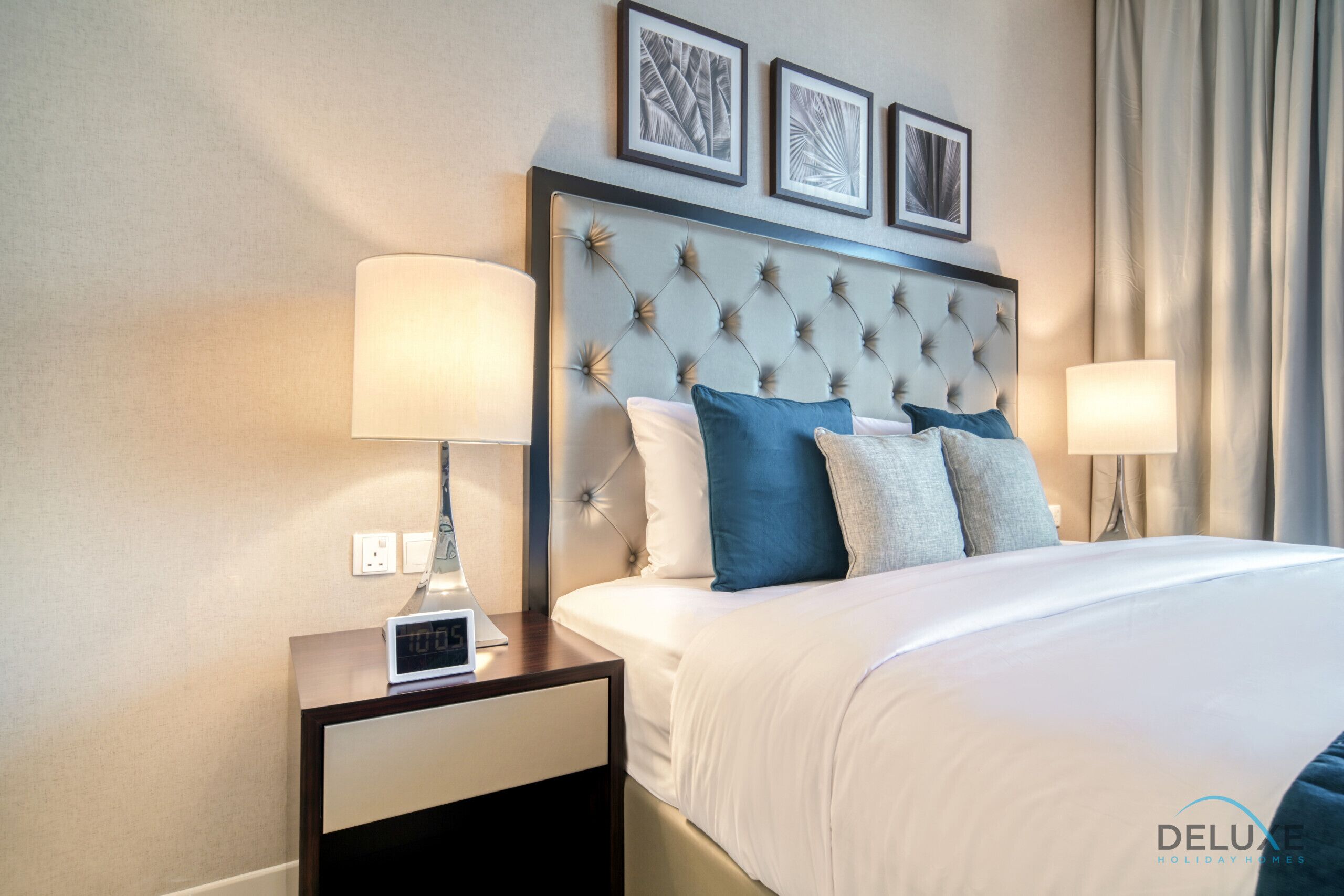Habitación de hotel con una cama grande, dos mesitas de noche, un reloj de pared y obras de arte enmarcadas sobre la cama.