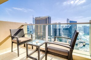 Un balcon agrémenté de meubles en osier et d’une table en verre, offrant une vue sur un paysage urbain dominé par des immeubles de grande hauteur.