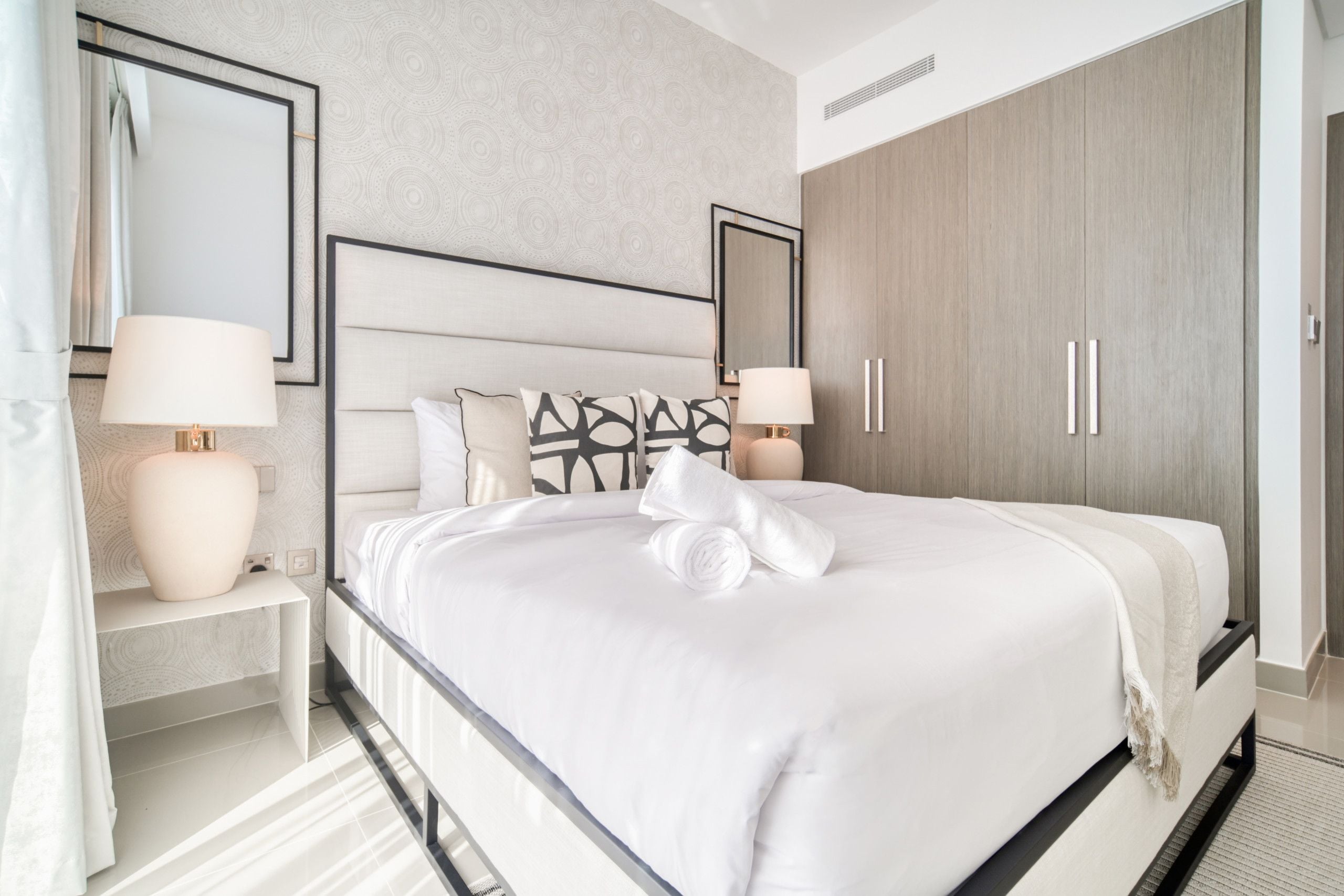 Habitación de hotel con una cama grande, dos mesitas de noche con lámparas, un armario y un espejo en la pared.