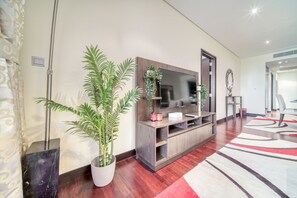Uma sala de estar moderna com uma televisão de tela plana grande, móvel para home theater de madeira, plantas em vasos e um tapete com padrão vermelho e branco.
