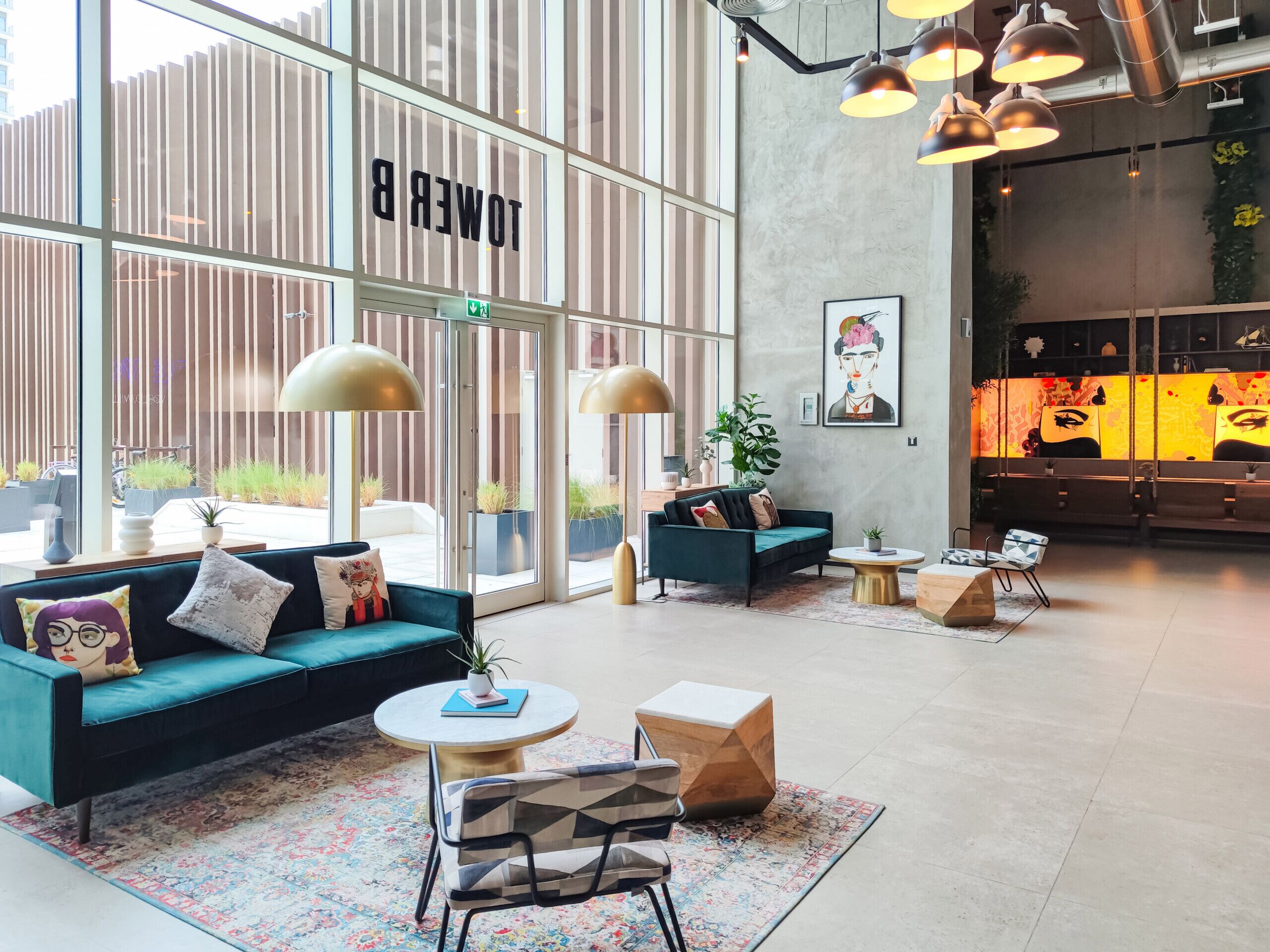 A modern lounge area with a teal sofa, round tables, and a coffee bar in the background.