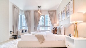 Ein modernes Schlafzimmer mit einem großen Bett, Nachttischen, einer Lampe und Blick auf die Stadt durch große Fenster.