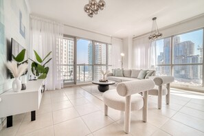 A modern living room with a sofa, a cat tree, a coffee table, and large windows offering a city view. - Glamorous 1BR at Residences 5 Downtown Dubai by Deluxe Holiday Homes (Dubai)