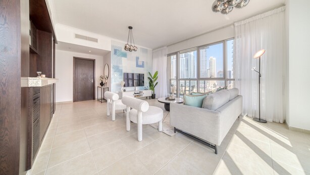 Ein modernes Wohnzimmer mit einer Couch, Sesseln und einem Fernseher. Ein großes Fenster bietet Blick auf die Stadt.