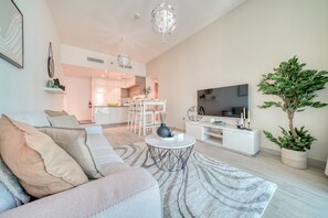 Una sala de estar moderna con un sofá, una mesa de centro y un televisor. Hay una zona de comedor con sillas y una mesa.
