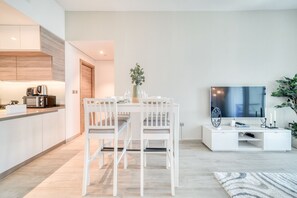 Ett modernt kök med vita köksskåp, en matplats med vita stolar, en platt-TV och en liten växt på bordet.