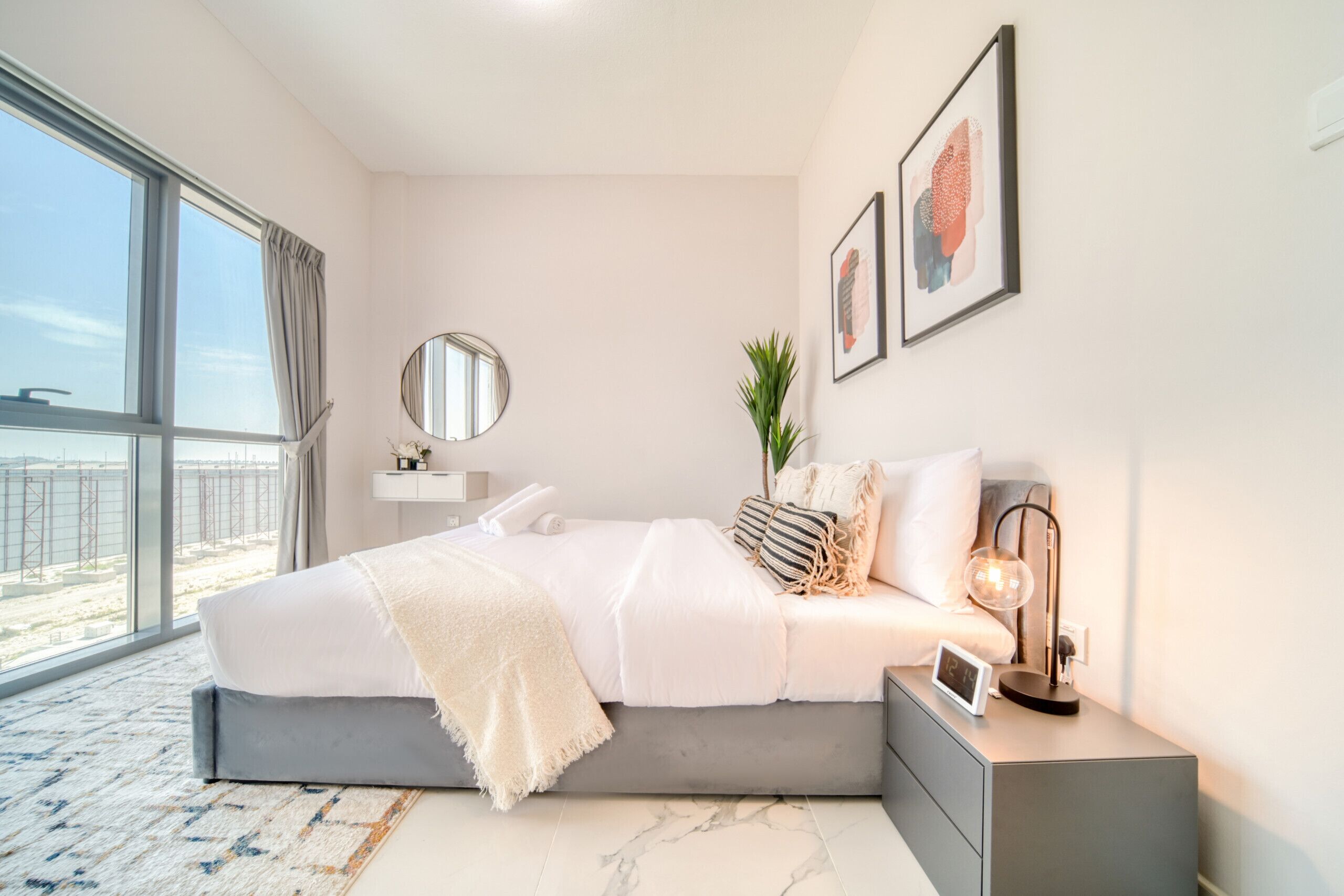 A modern bedroom with a large bed, bedside tables, a mirror, and artwork on the walls.